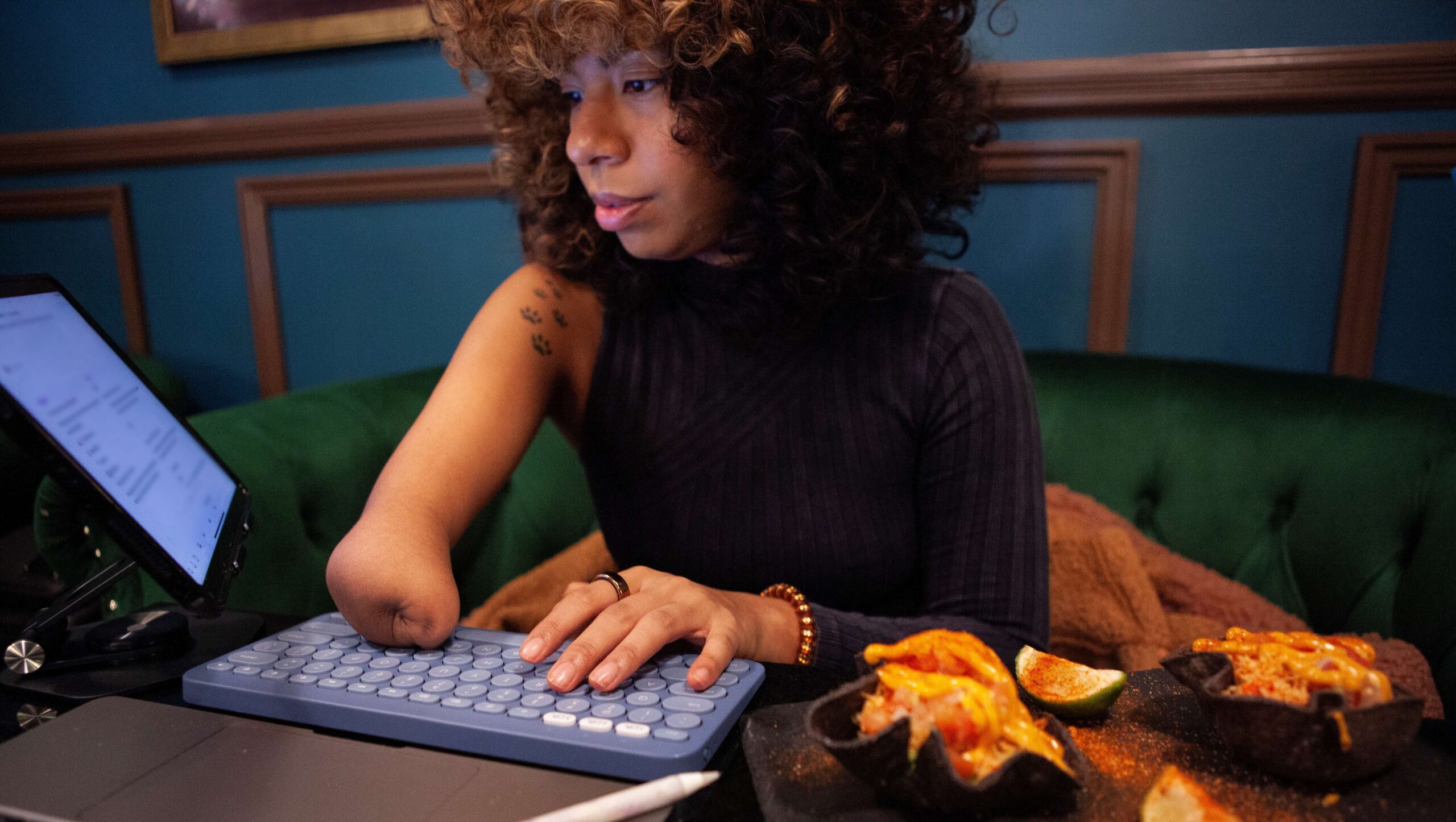 A woman with a lower arm amputation types on her keyboard while eating ripe fruit.