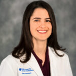 Headshot of Dana Rubenstein. A white woman with long brown hair wearing scrubs.