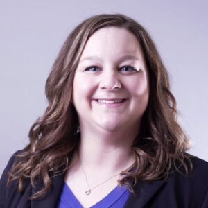 Headshot - Kaley Graves. White woman with long wavy brown hair, wearing a purple shirt and blazer.