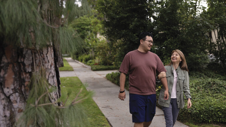 California_Los Angeles_APIDC_Brown-Shirt, Sage-Jacket_8846_v1_Web A man walks arm in arm down the sidewalk with a companion.